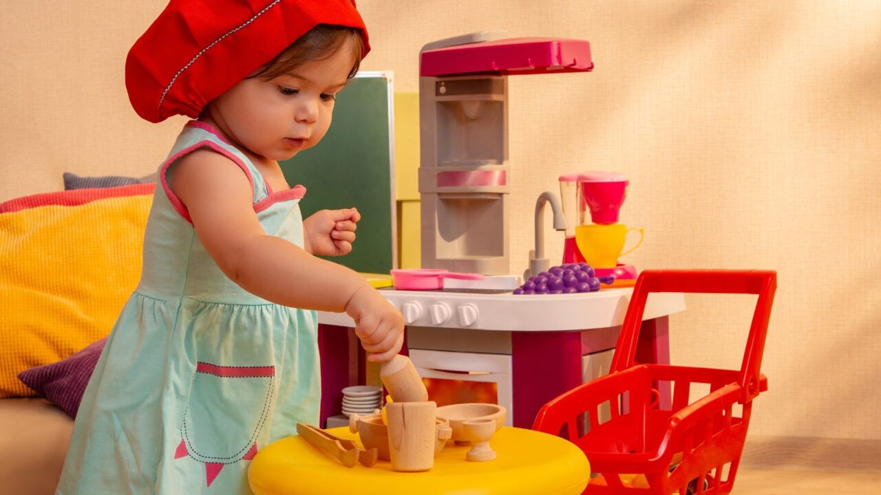 A little girl playing with kitchen set in her room.