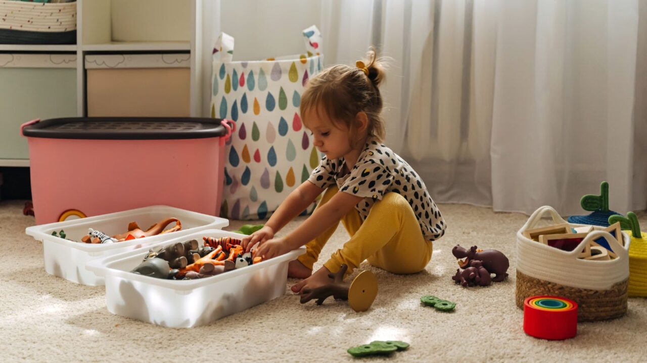 A little child putting toys in a clear basket.