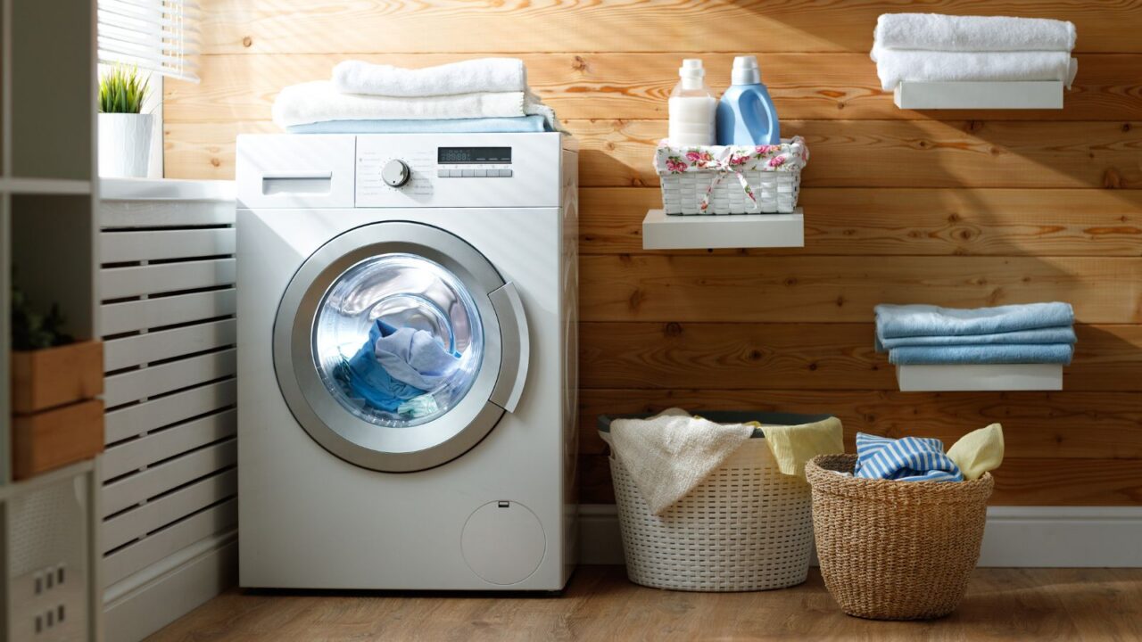 A laundry room with a washing machine, floating shelves, and baskets with clothes.