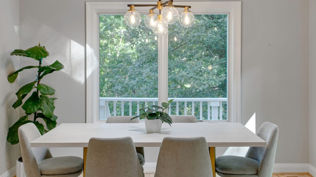 A dining room interior with a white dining table, chairs, chandelier, a fiddle leaf fig , and a small plant pot on the table.