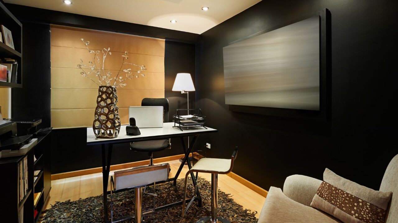 A stylish home office interior with a sofa, bookshelf, a sculptural flower vase, table, chairs, rug, and a table lamp.