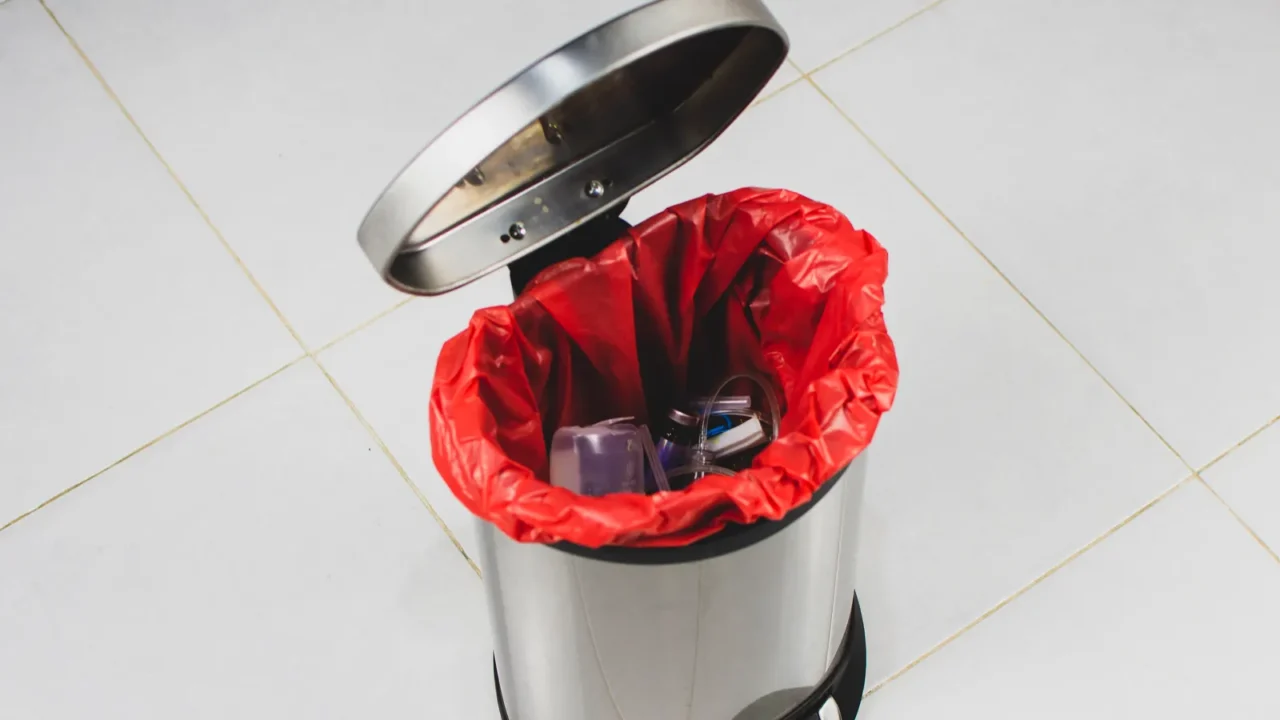 A stainless steel trash can with a red liner, partially filled with assorted trash, viewed from above.