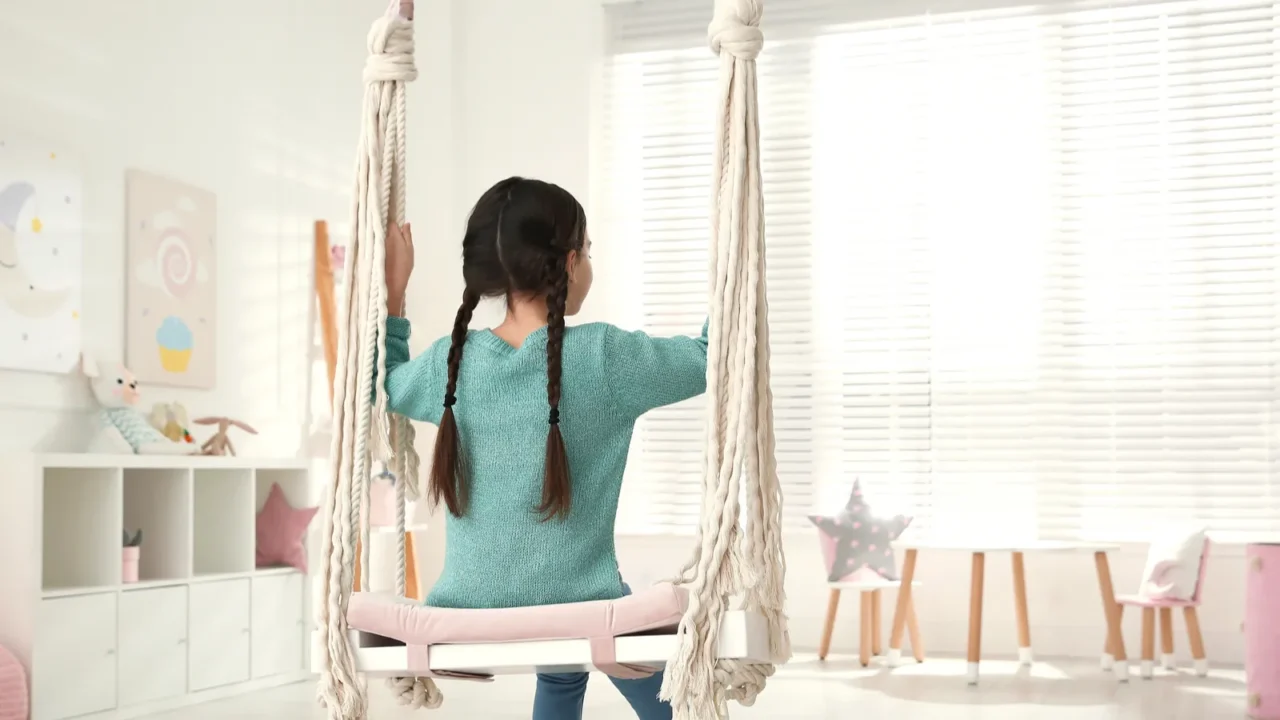 A girl swinging on a DIY swing made from wooden board, rope, and a cushion.