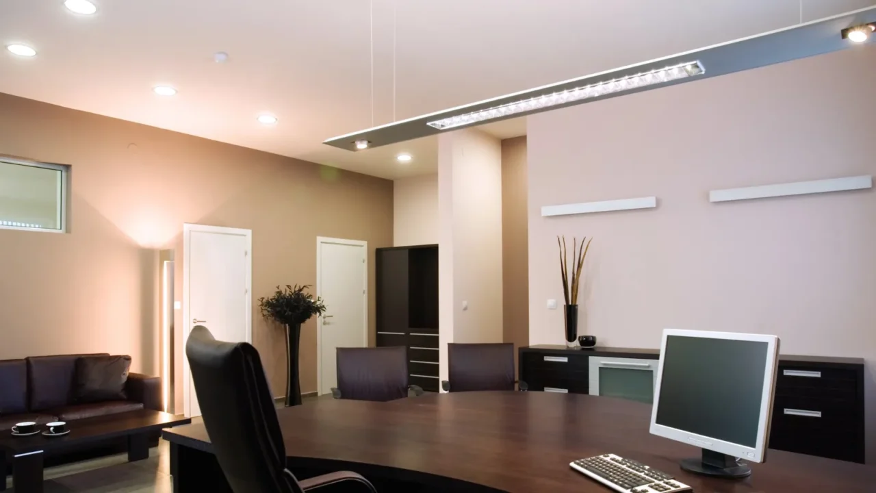 An elegant and luxury office interior with ergonomic chairs, dark wooden table, leather sofa, and sleek linear pendant light.