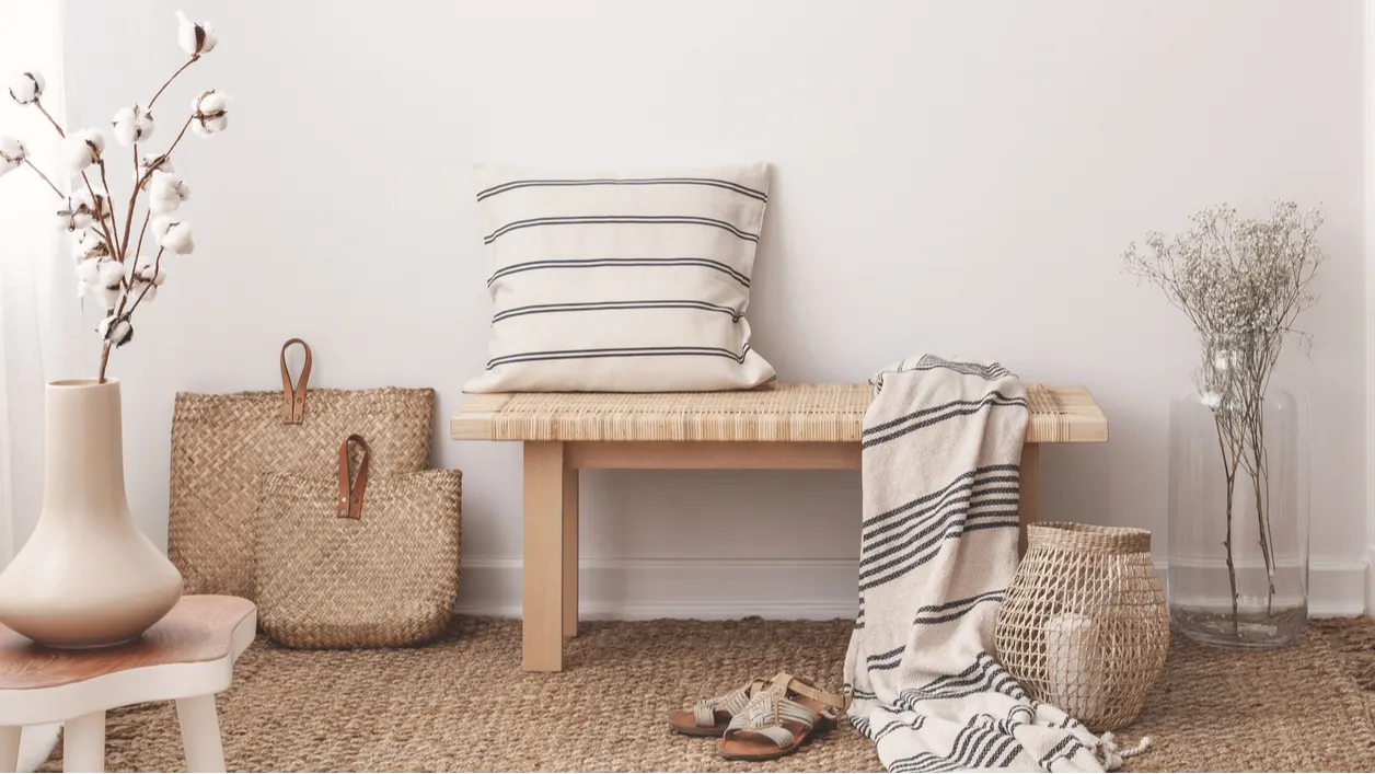 A minimalist entryway featuring a wooden bench, striped pillow, and woven baskets.