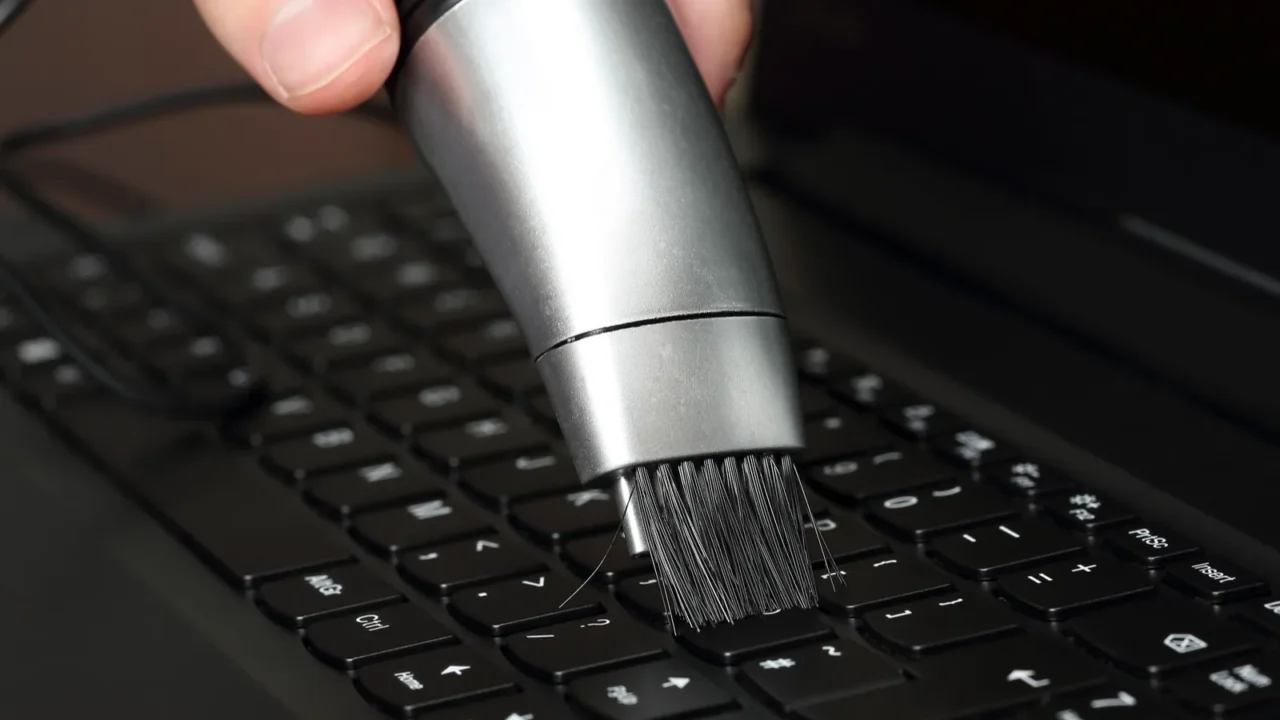 hand with mini vacuum cleaner on laptop keyboard