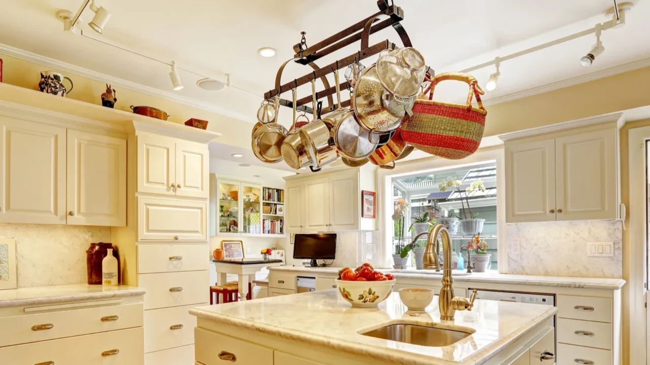 A kitchen interior with hanging pot rack with various pots and pans, positioned above a marble-topped island with a sink.