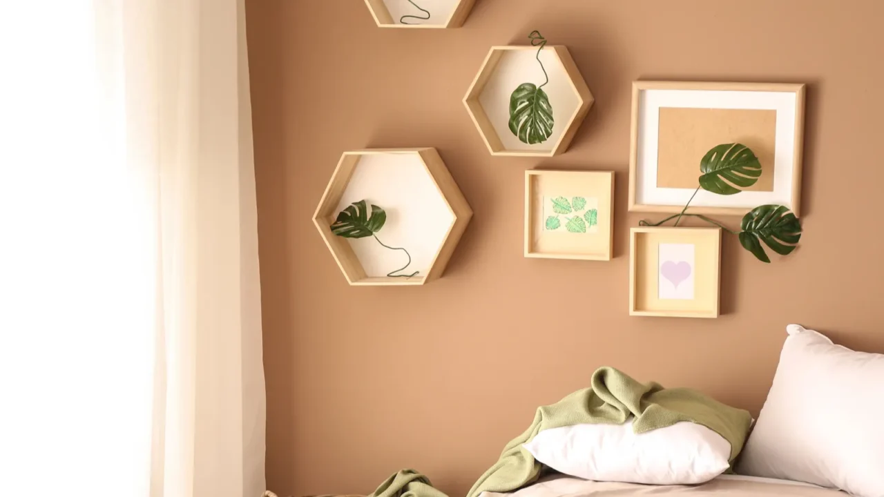 A beige wall with decorative hexagonal frames and green foliage accents, alongside a bed.