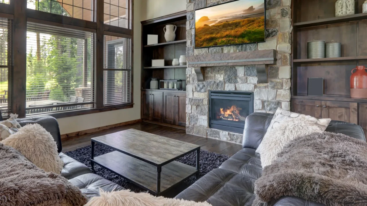 A rustic living area with a dark leather sofa, stone fireplace, wooden shelves with vases, and a wooden coffee table.