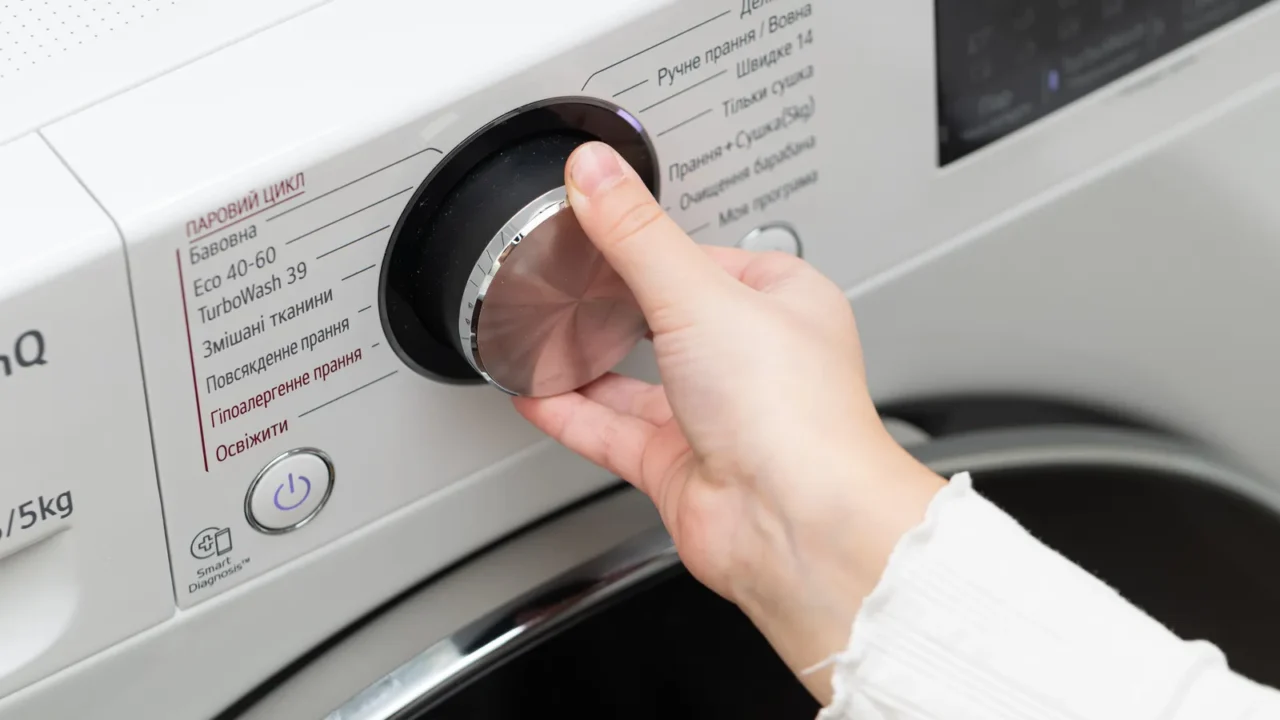 A hand turning the dial on a washing machine's control panel.