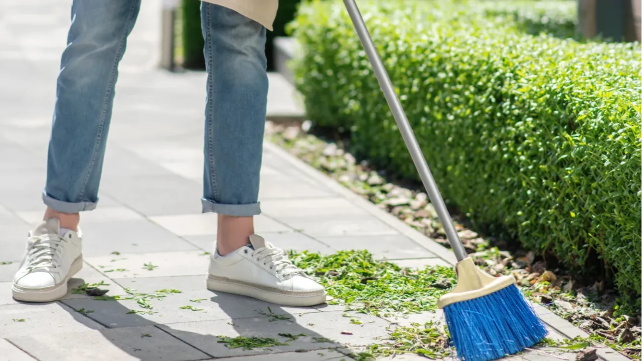 male in protective gloves and apron sweeping leaves with broom