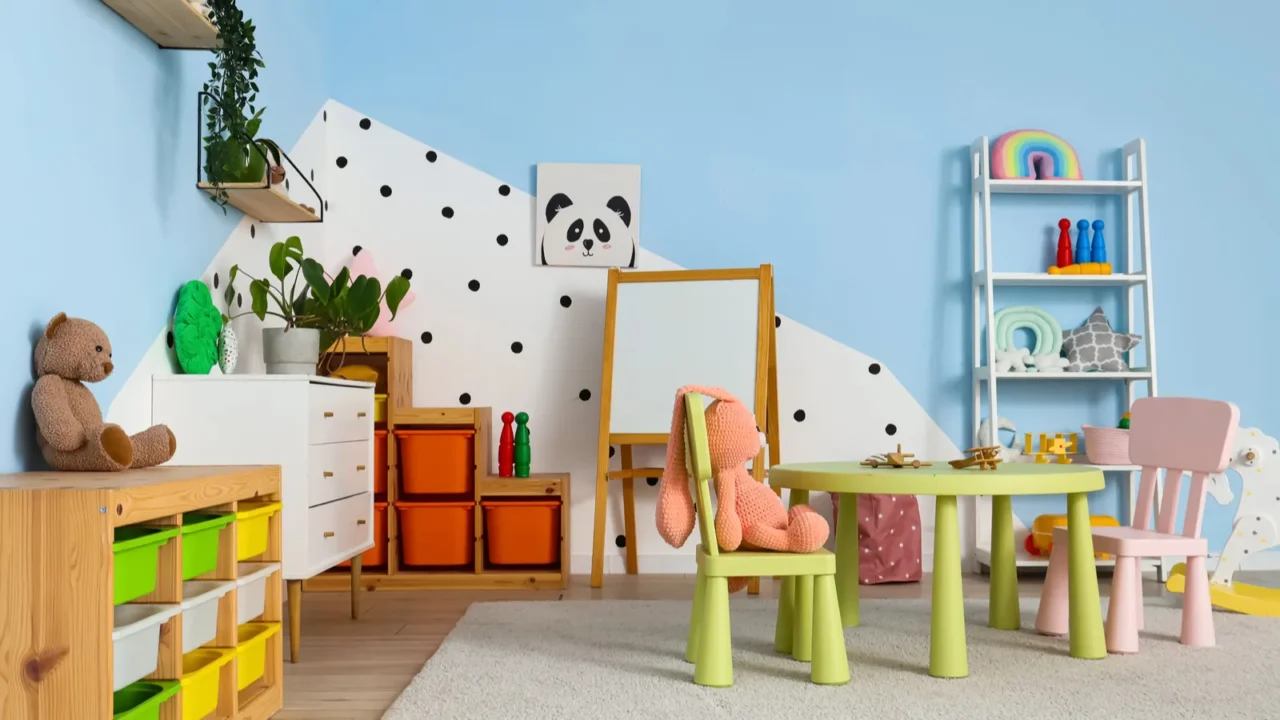 A playroom interior with a wooden shelf, white board, stuff toys, a white open shelf with toys, and a poster on a blue wall.