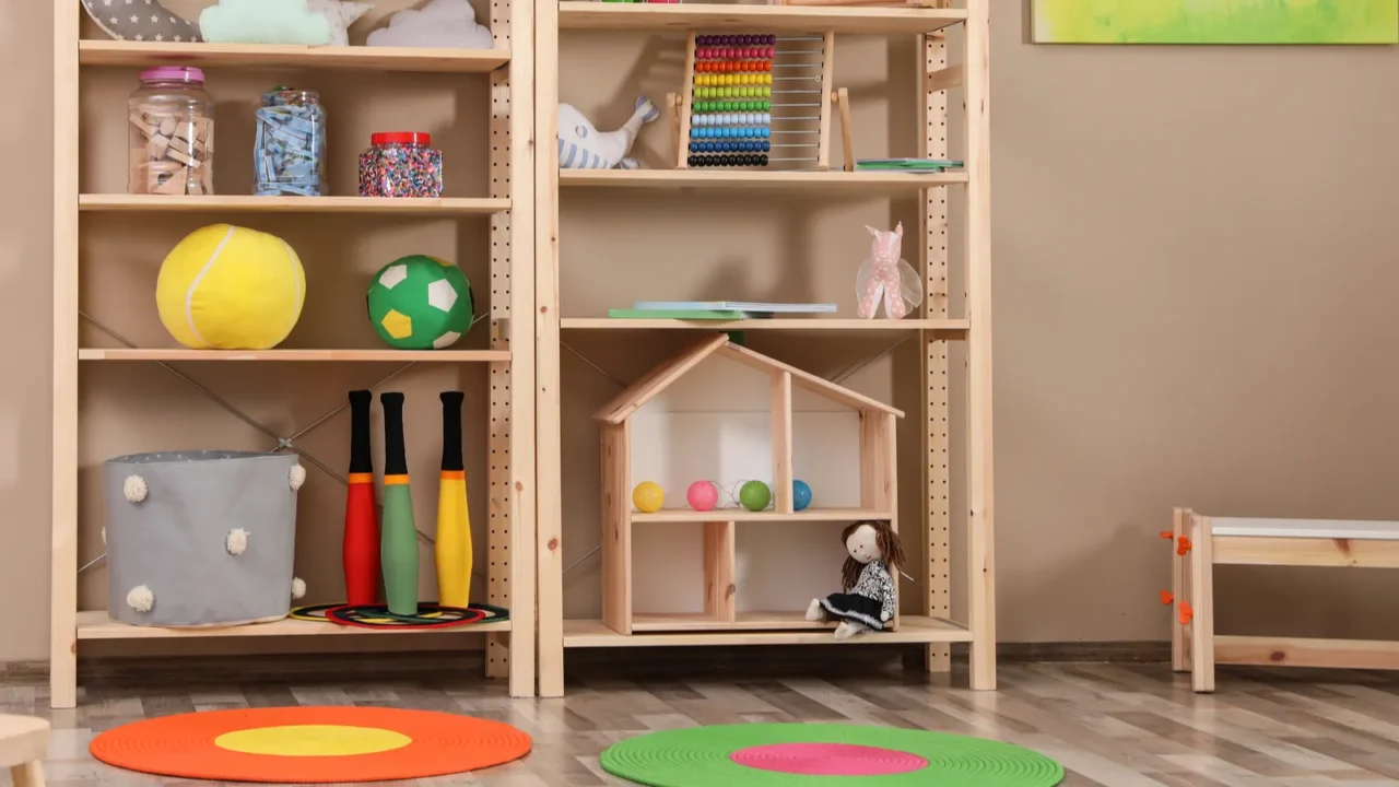 A playroom interior with colorful rug, wooden bench, and a wooden toy shelf in front of a beige wall.