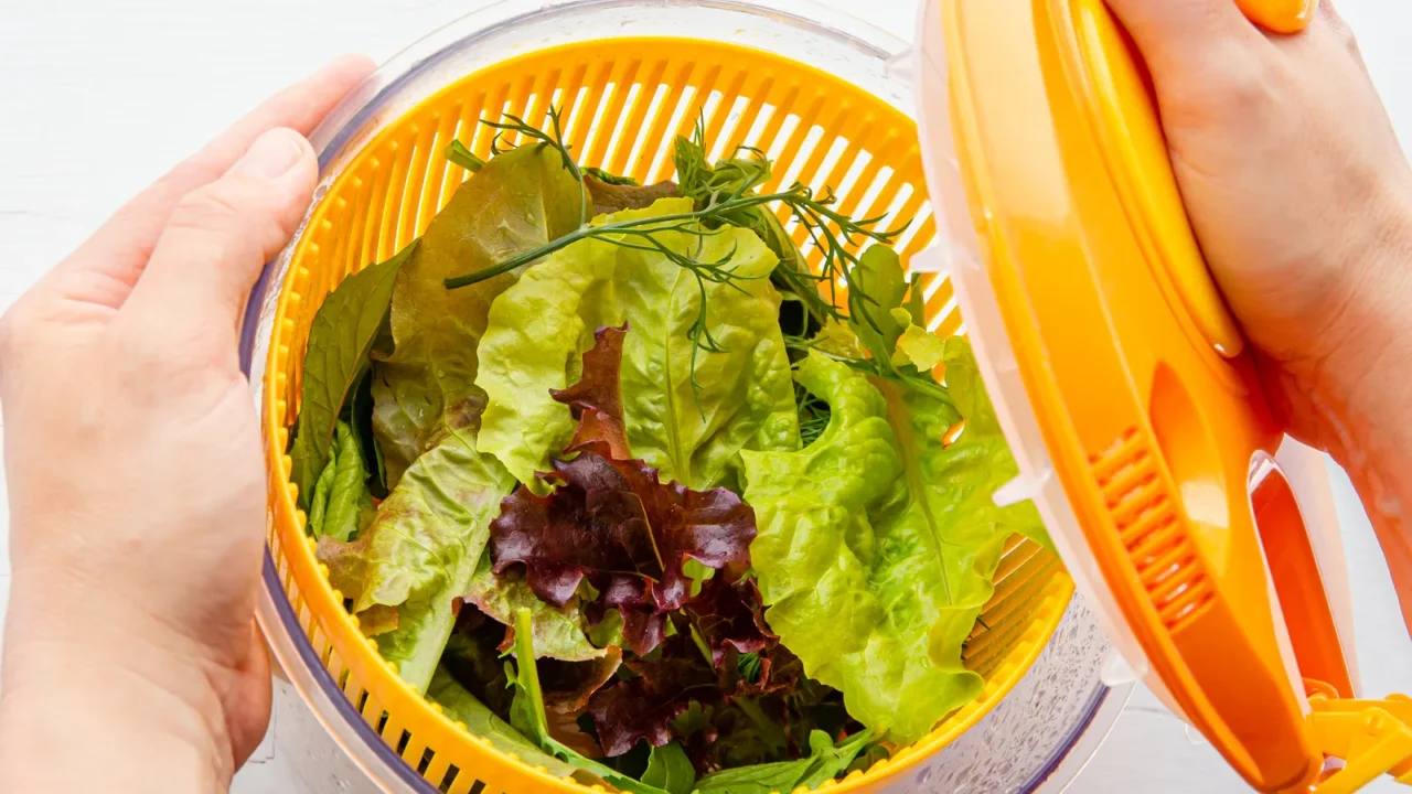 A woman closing the lid of a salad spinner with greens in it.