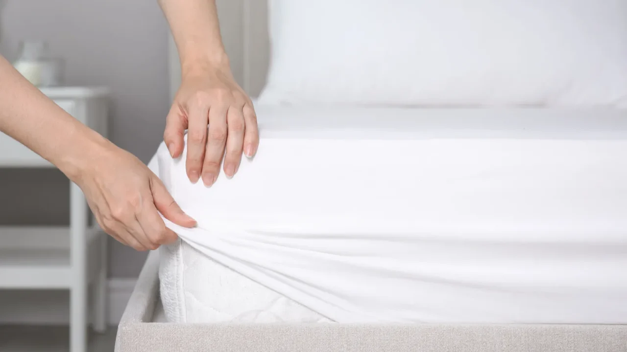 woman putting white fitted sheet over mattress on bed indoors