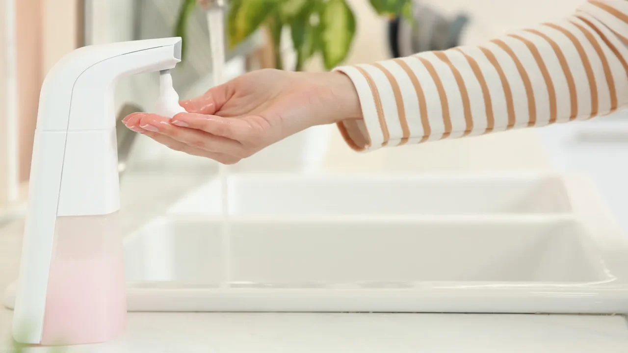 woman using automatic soap dispenser in kitchen closeup