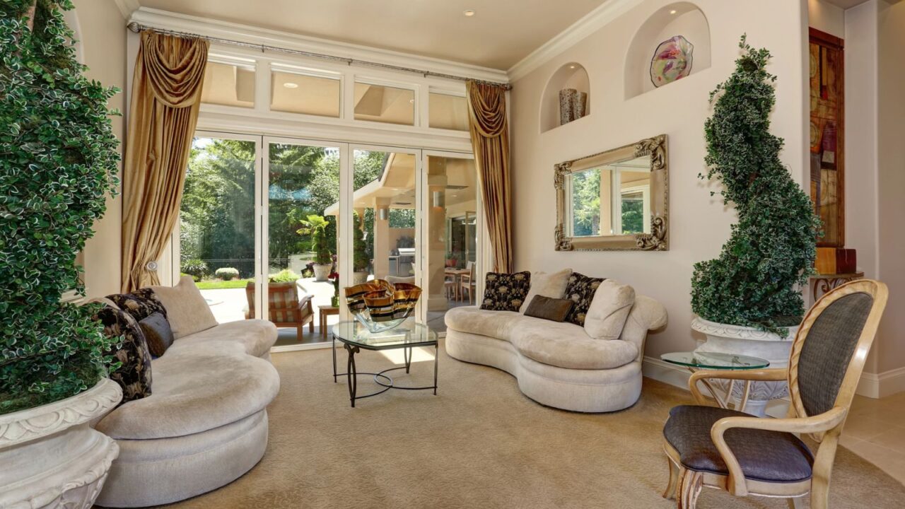 A luxurious living room features a curved sofa, elegant decor, large windows with greenery outside, and a stylish glass coffee table.