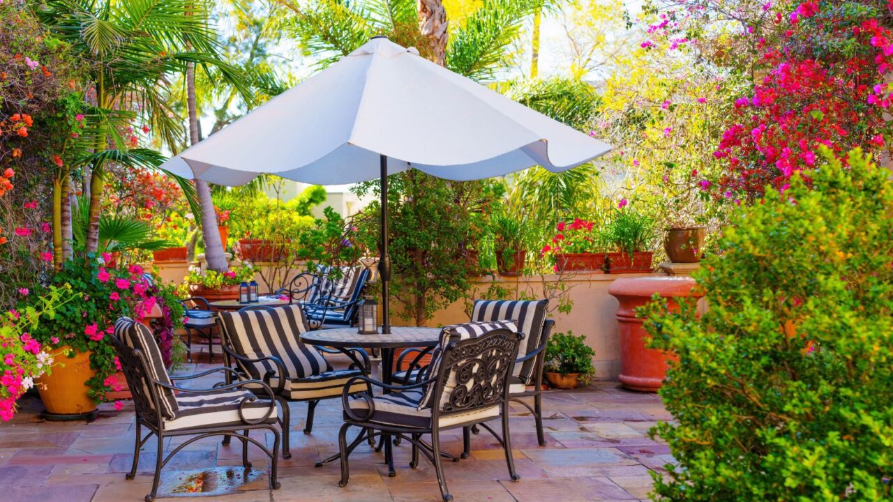 A garden with a dining set under a white umbrella surrounded by plants.