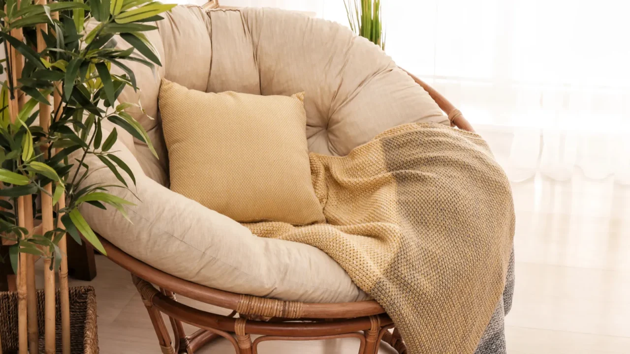 A cozy armchair with cushion and throw blanket with potted plant beside it.
