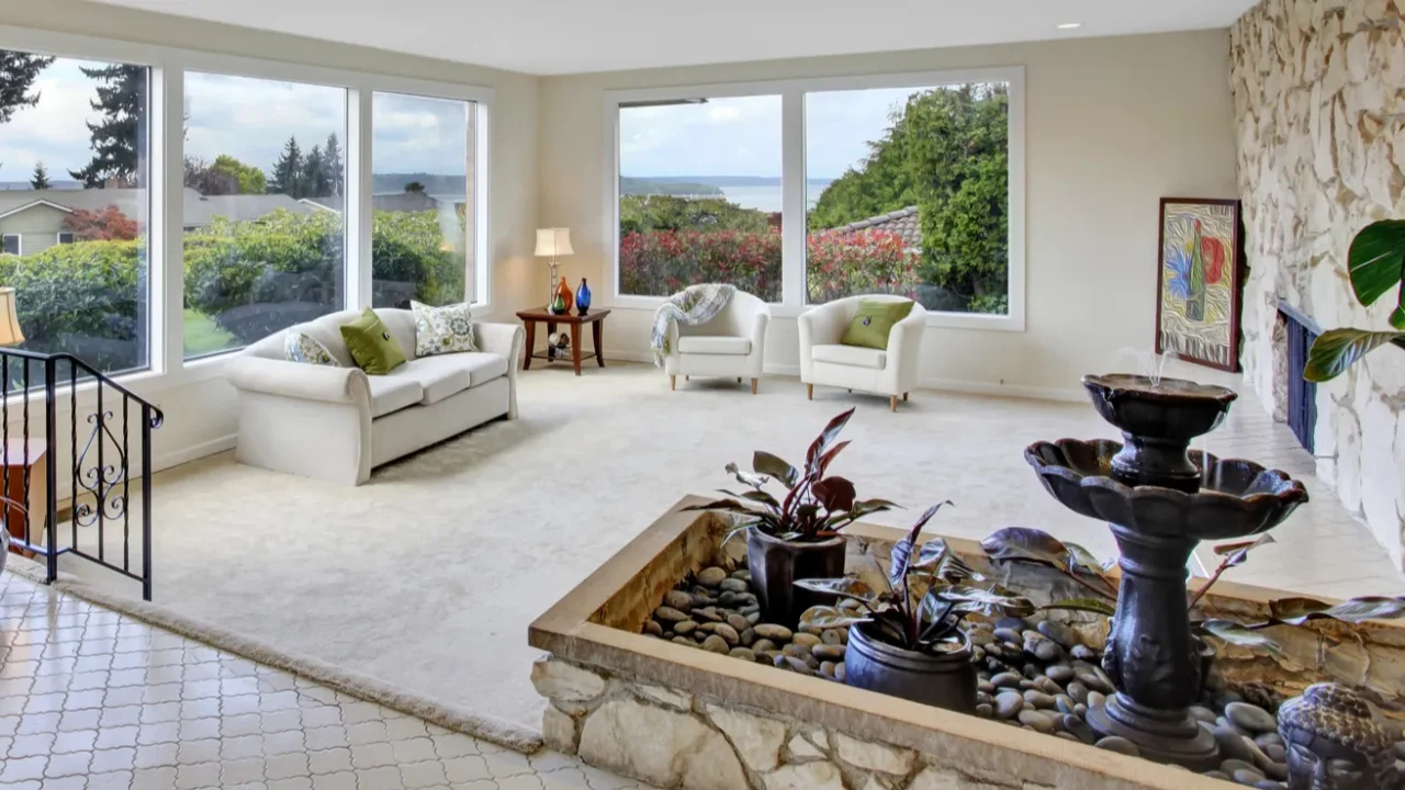 A luxury living room interior with sofa, wooden side table, indoor fountain, stone accent wall, and artwork.