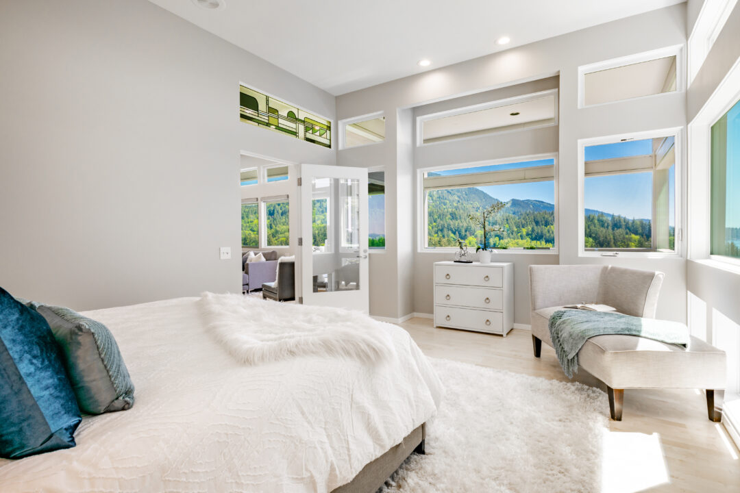 A bright, modern bedroom showcases a comfy bed with decorative pillows and large windows revealing a scenic view.