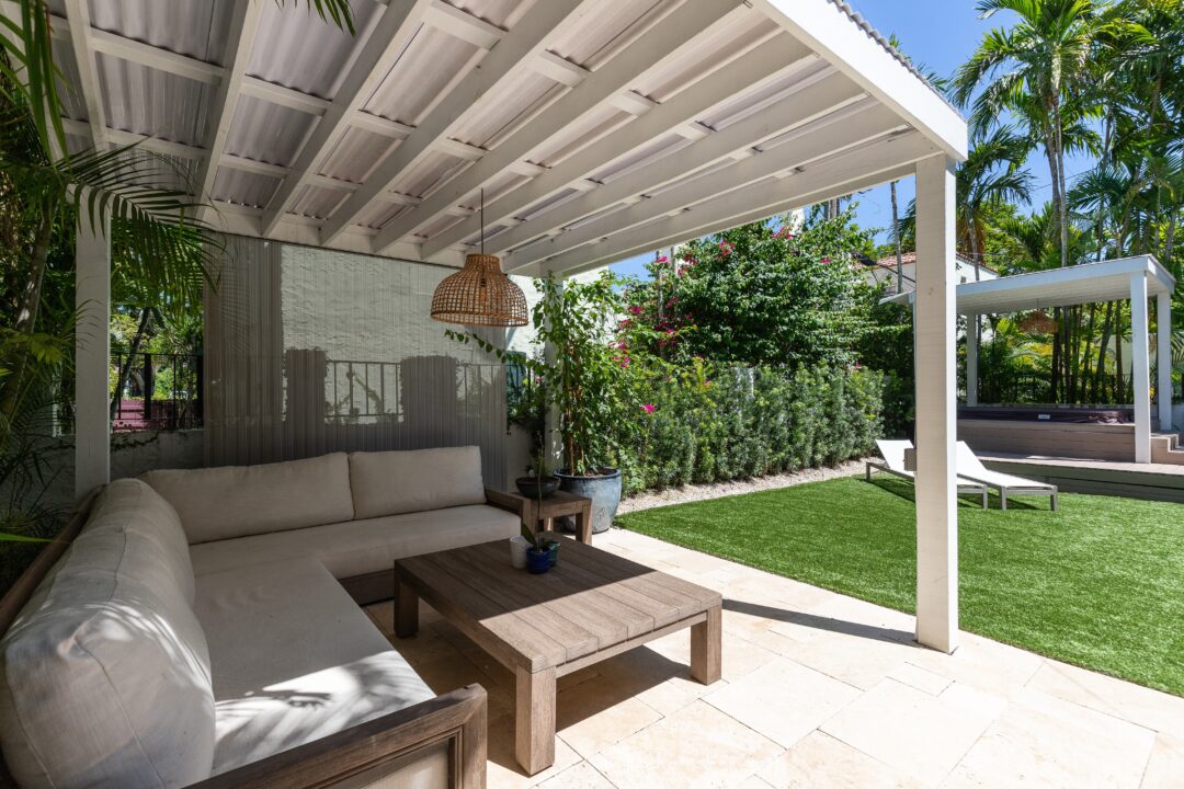 Outdoor - A cozy outdoor lounge area includes a comfortable sofa, wooden coffee table, and lush greenery surrounding the space.