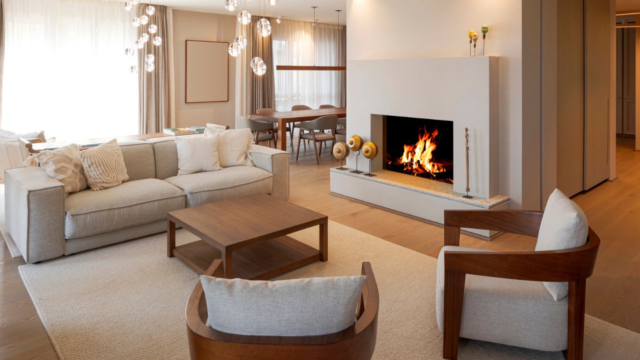 A modern luxurious open concept living space interior with sofa, wooden armchairs, coffee table, fireplace, chandeliers, and dining set.
