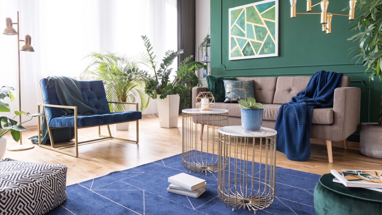 A bright living room with green walls, a beige sofa, blue armchair, and metal accents.