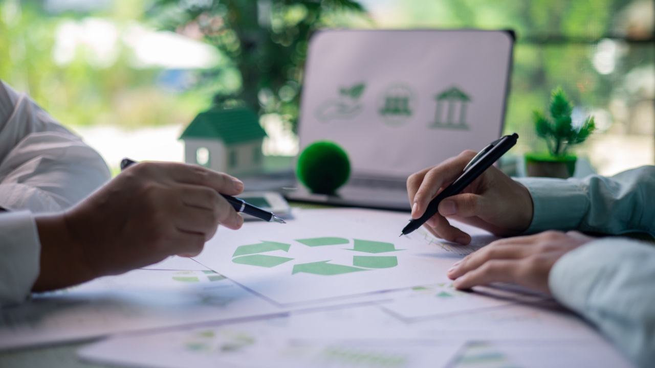 Two people discussing eco-friendly designs with paperwork and a model house.
