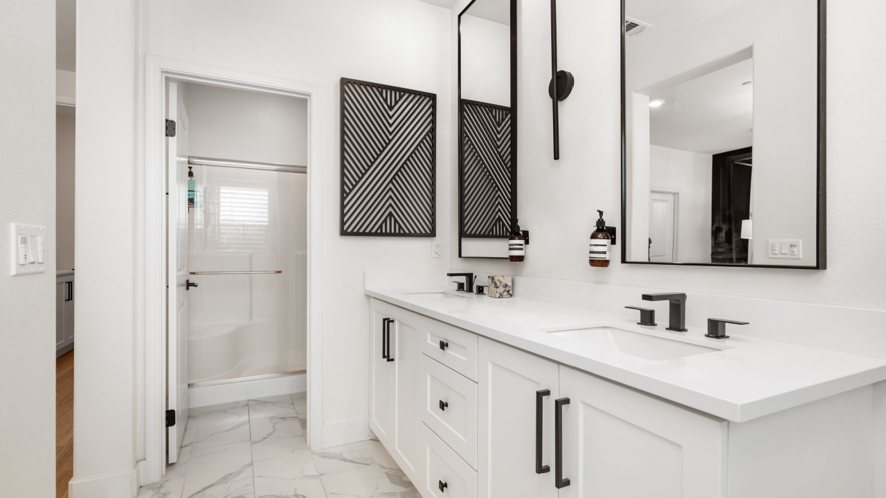A minimalist white bathroom with black accents and large mirrors.