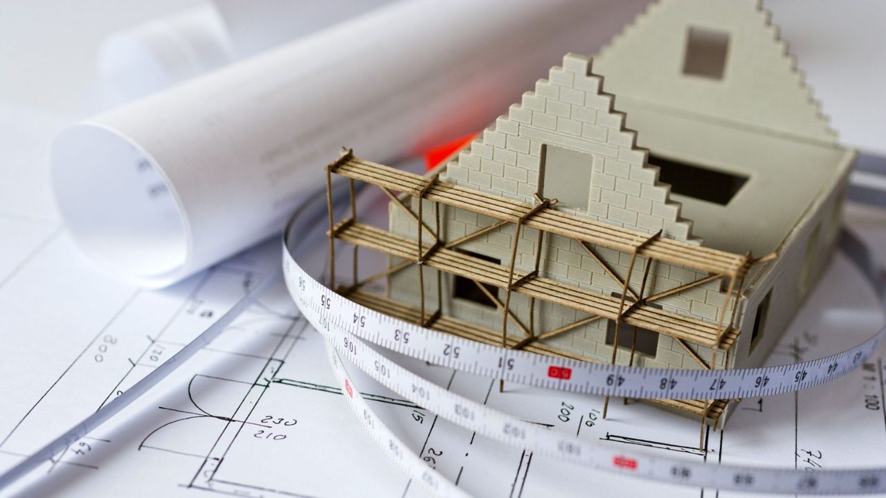 An architectural plans and a model house with measuring tools.