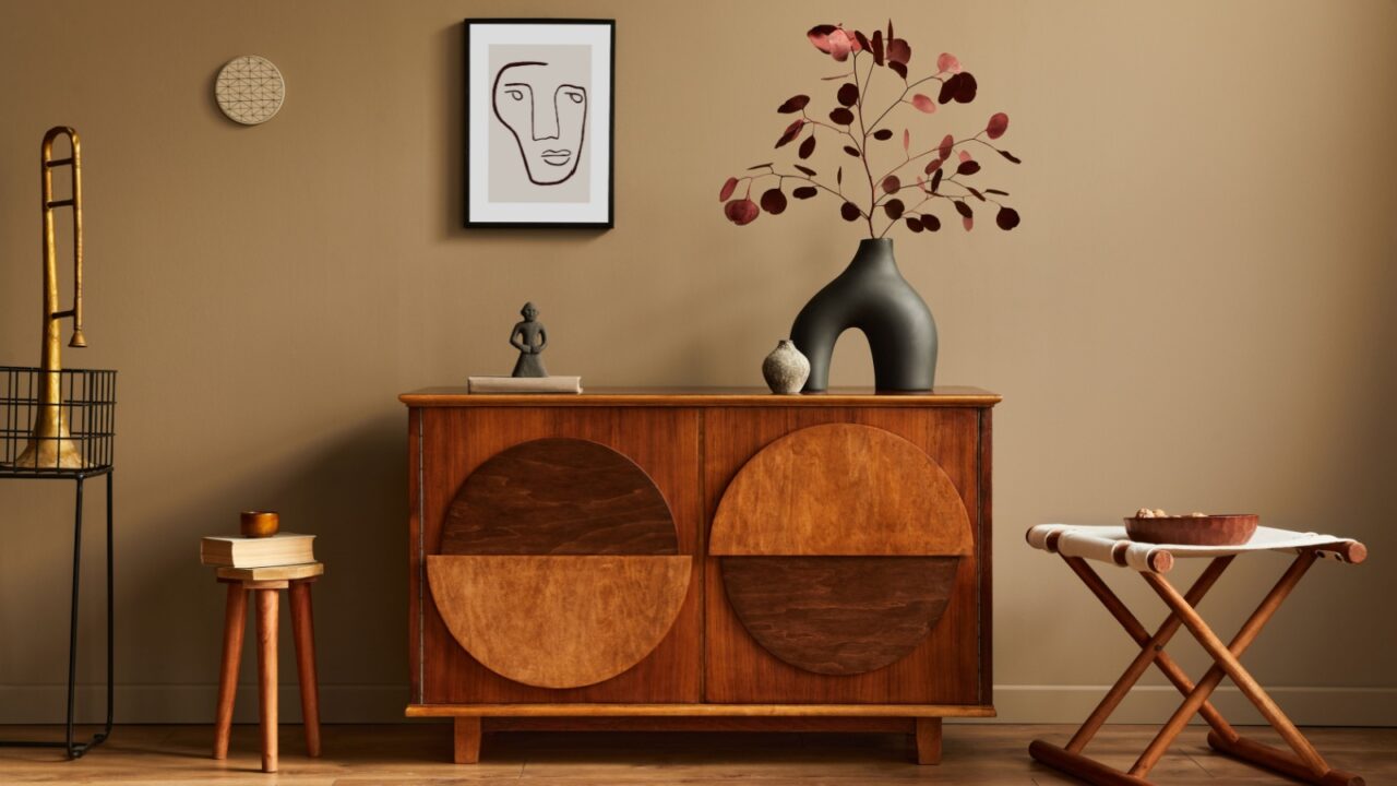 A living room interior with a wooden stool, wooden console with decorative flower vase, and a framed poster on the wall.