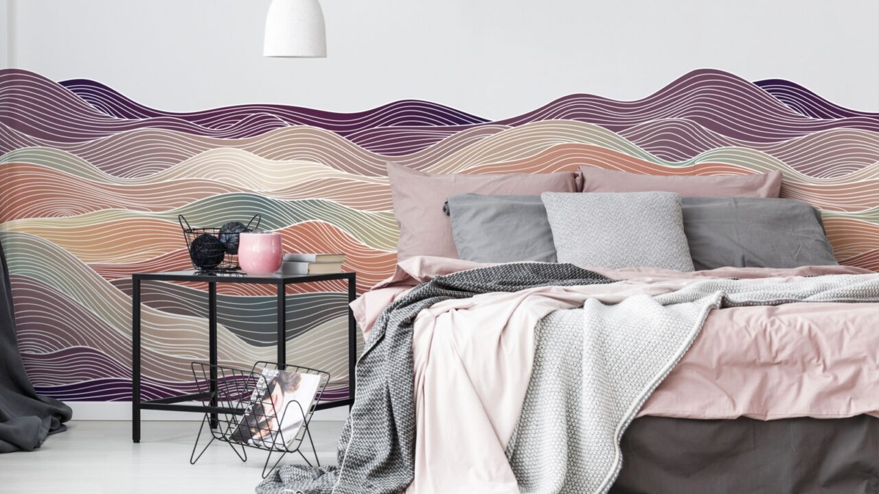A modern bedroom with colorful mural walls, pink and gray bedding, and a tidy bedside table.
