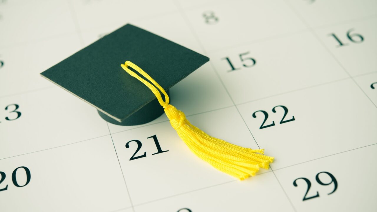 A calendar in the background with a small green graduation cap on it.