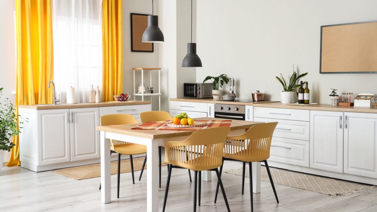 Interior of modern kitchen with white counters, dining table, yellow curtains, chairs and lamp