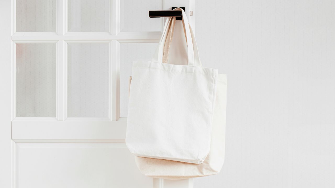 A white tote bag hanging on a door with a window.