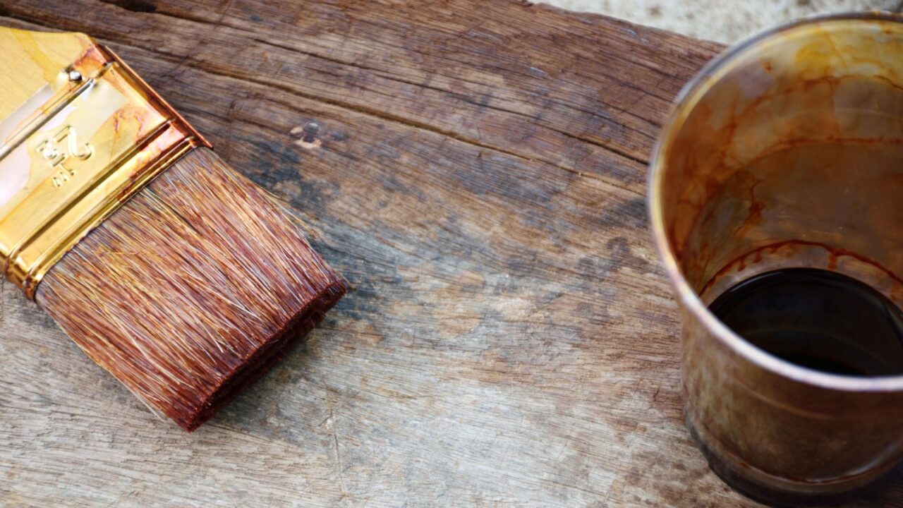 A brush and a glass with wood sealant placed on a wooden table.
