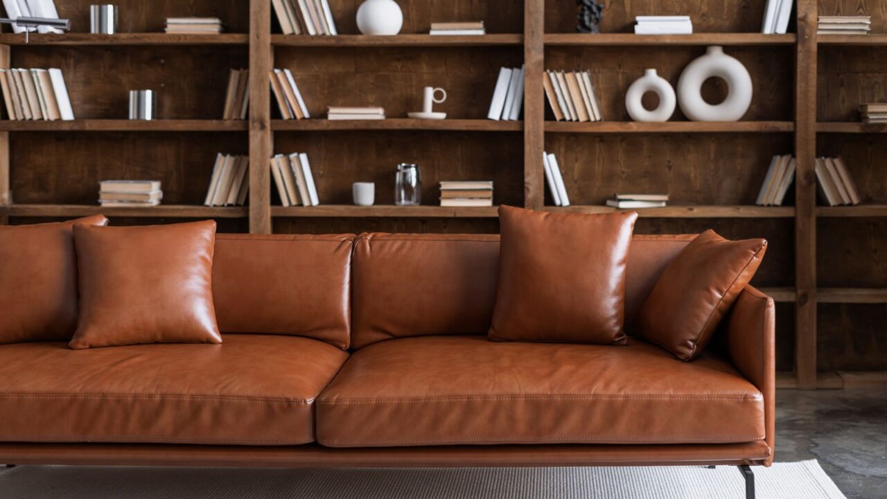 A leather sofa with cushions in front of a wooden bookshelf with books and sculpted decor accents.
