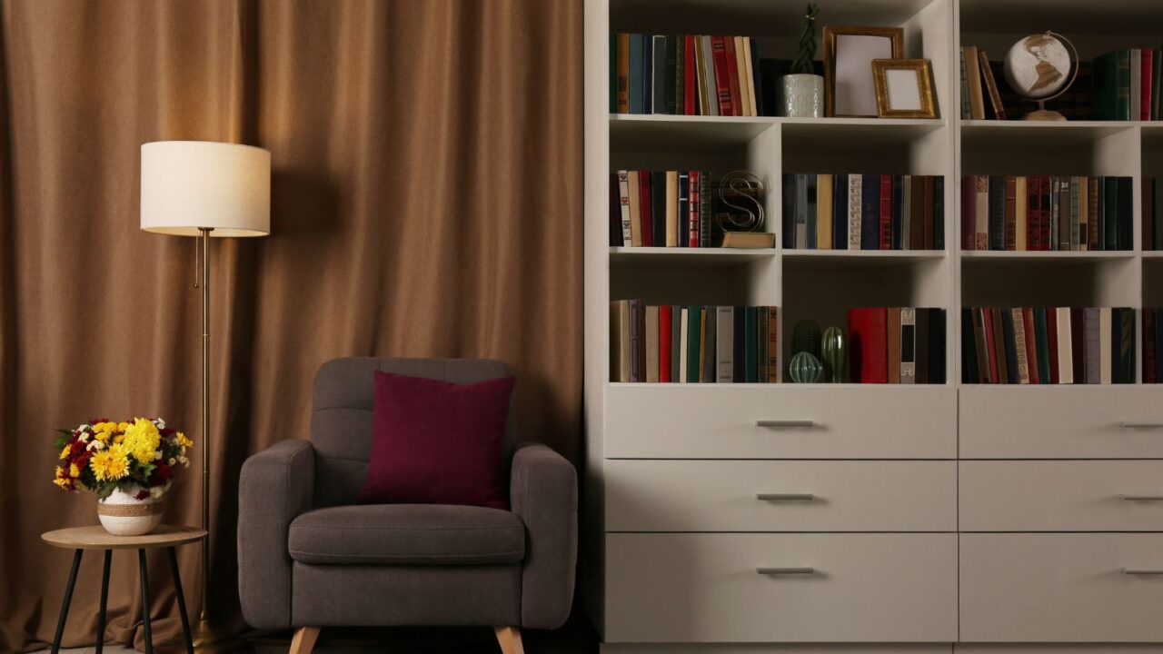 A white bookshelf with frames, books, and decor accents with a cozy armchair and floor lamp beside it.