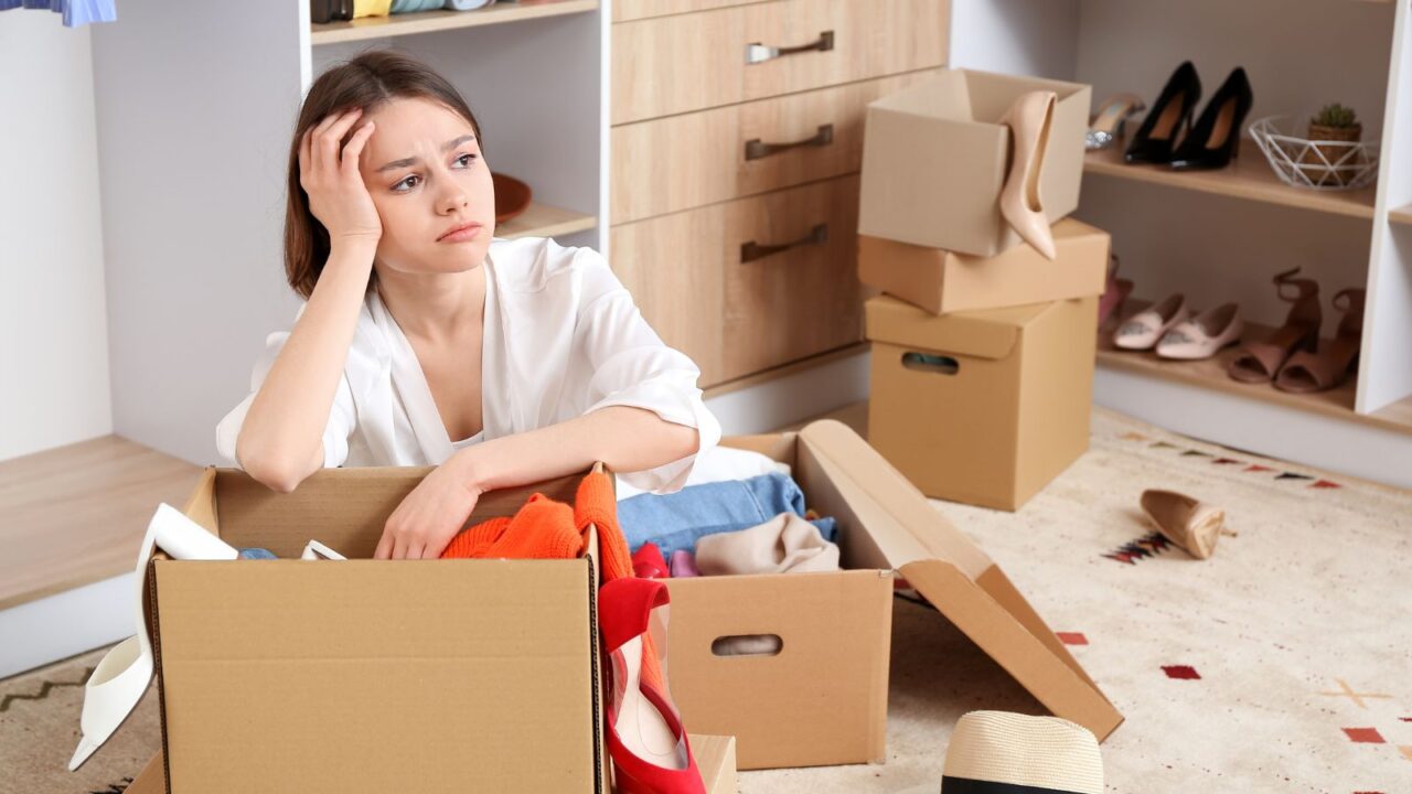 A lady looking upset while decluttering the wardrobe with storage boxes in front of her.