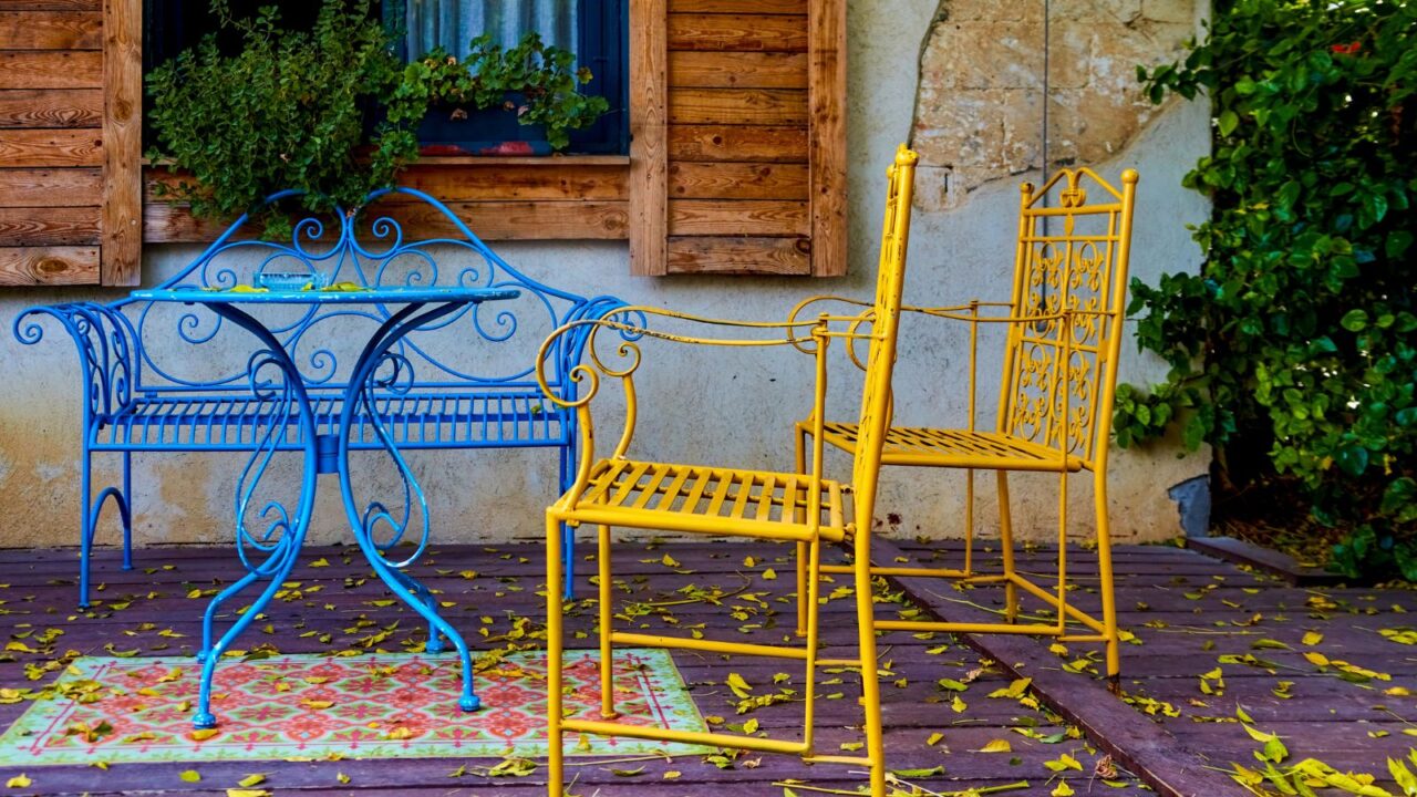 A stylish patio with blue and yellow dining set on a wooden floor in front of a wooden window.