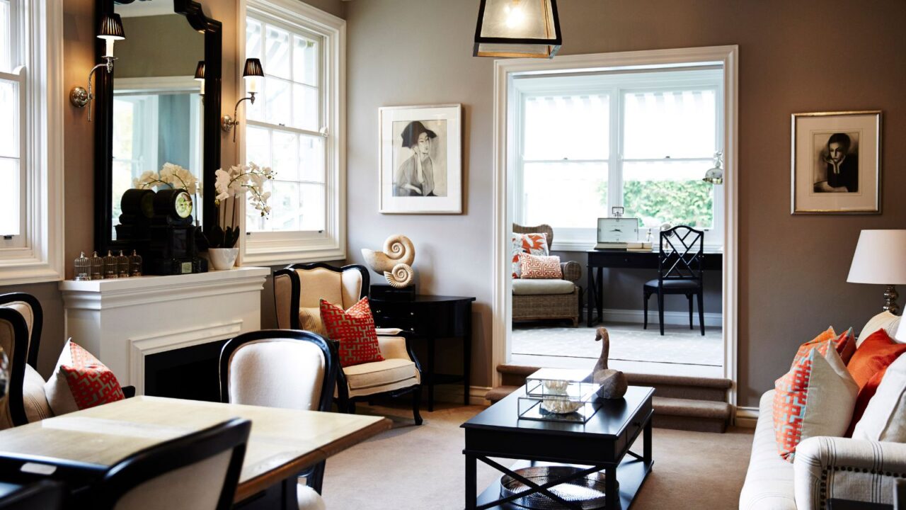 A living room interior with taupe walls, a dining set, wooden coffee table, sofa, and framed sketched portraits on the wall.