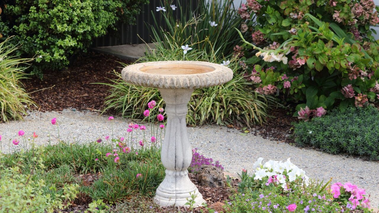 A beautiful garden with a weathered stone birdbath surrounded by flowering plants.