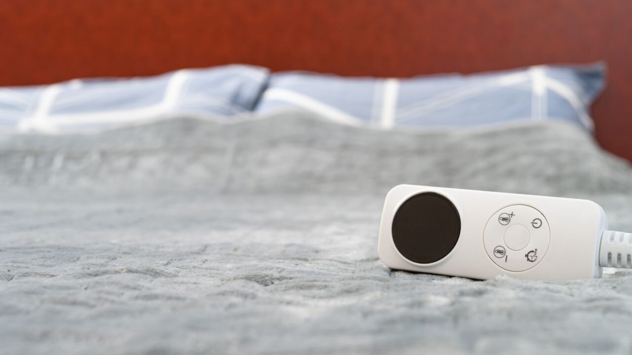 A gray electric blanket with a controller on the bed.