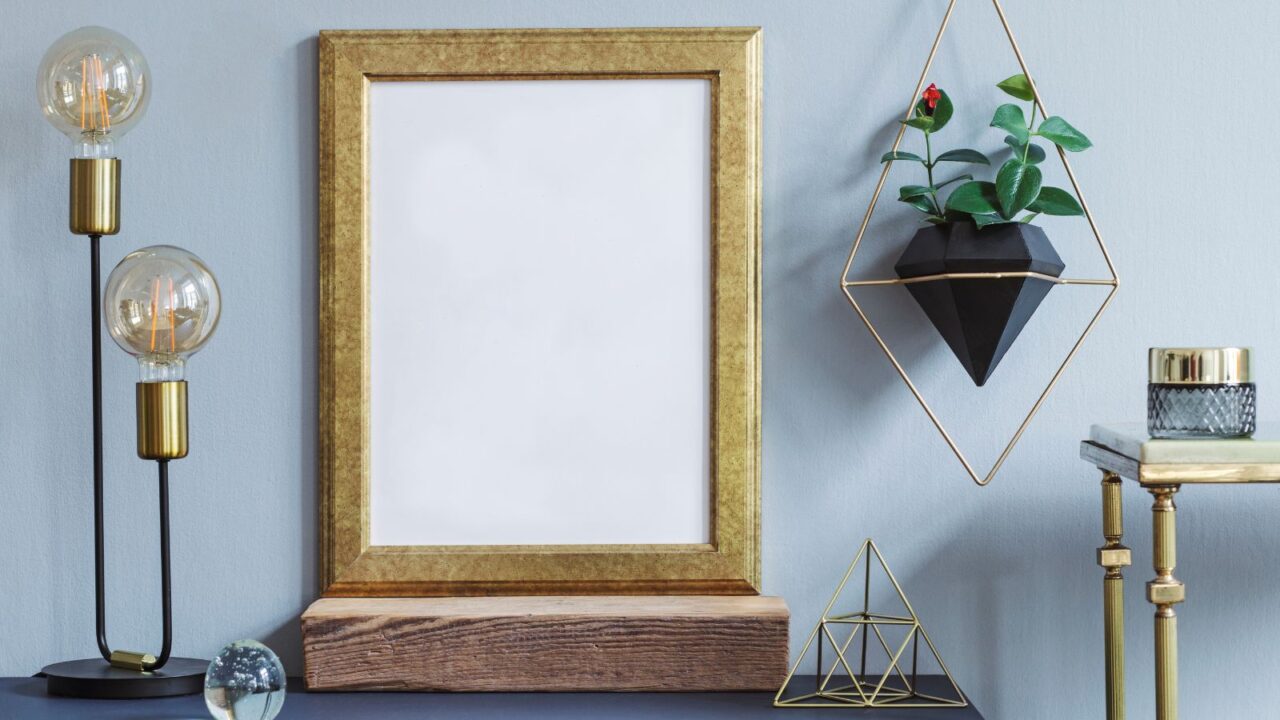 A console table with table lamp, pyramid, and a golden frame art in front of a blue wall.