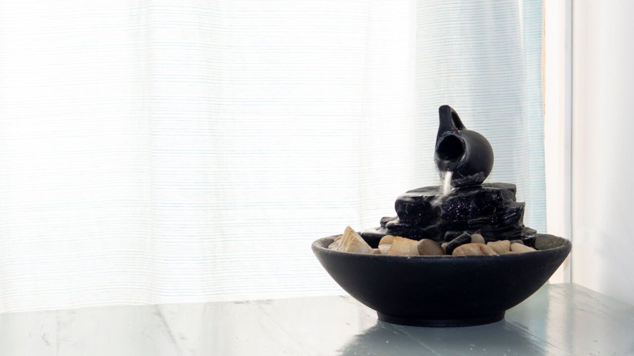 An indoor mini fountain on a white wooden table near a window.