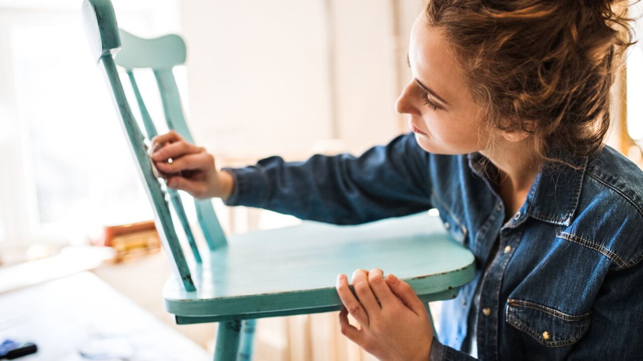 A woman inspecting a blue wooden chair.