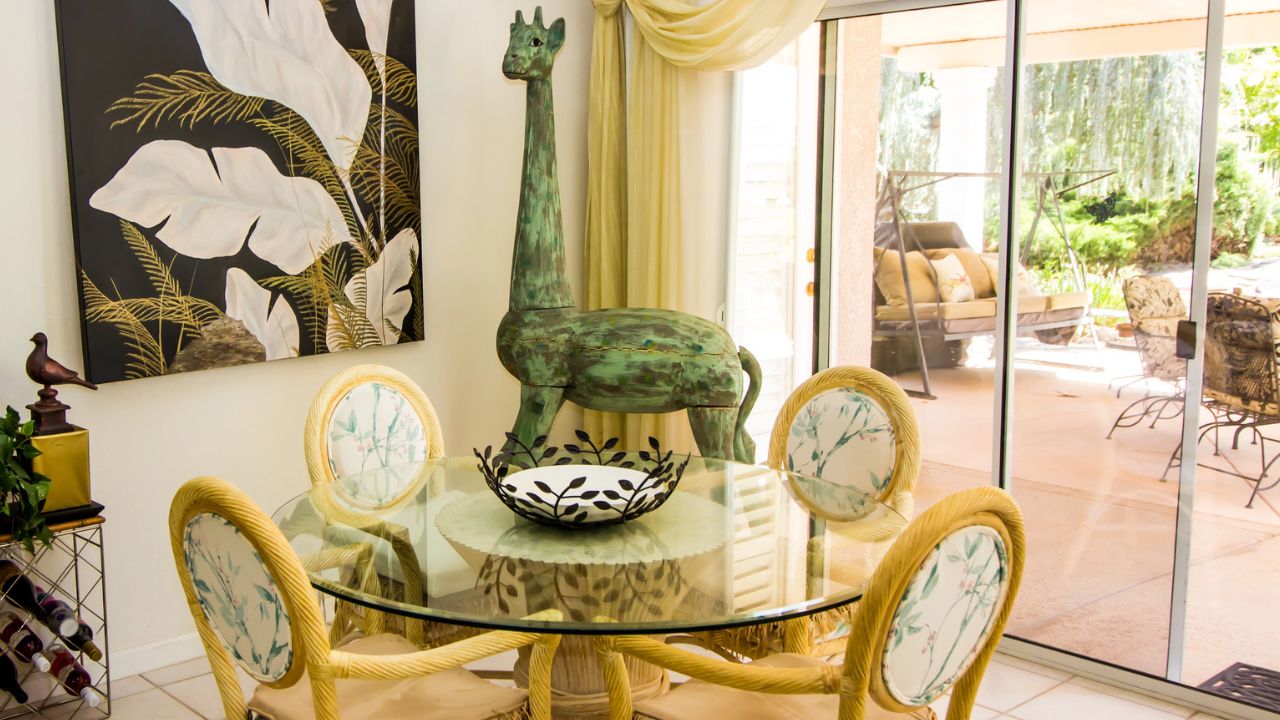 A dining area featuring a glass table, decorative giraffe sculpture, and tropical artwork.
