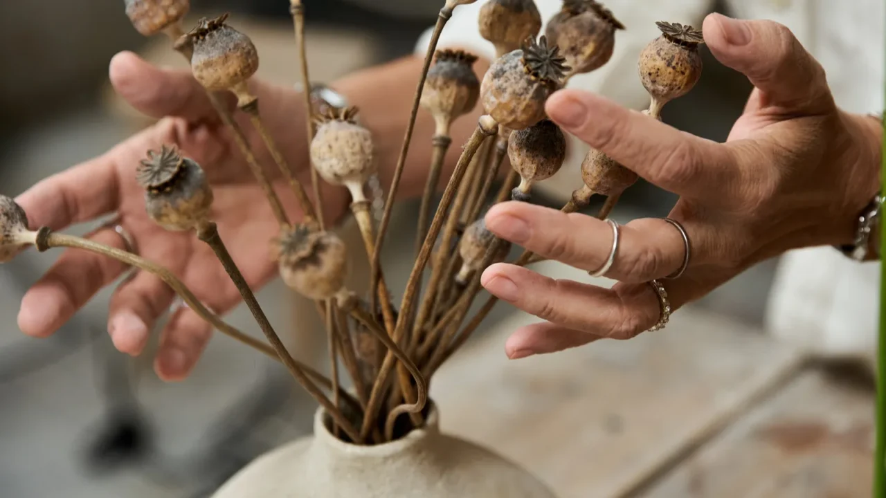 a mature woman delicately arranges dried poppy flowers in a
