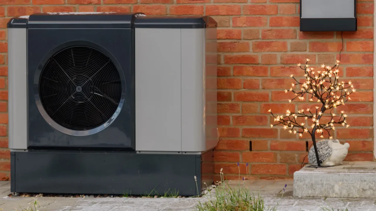 An outdoor heat pump unit beside a brick wall, designed for heating and cooling.